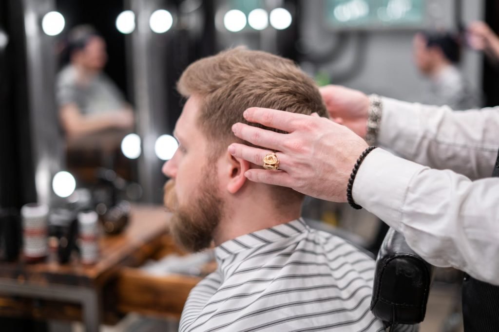 Barber styling a bearded mans hair in a modern barbershop setting.